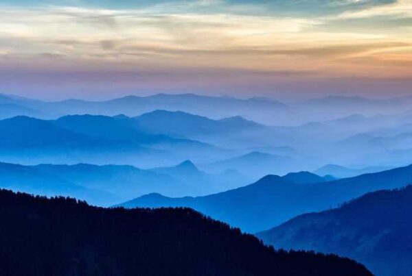 A range of hills and mountains with mist and cloud in a variety of blues and oranges