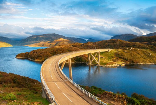 a road bridge over water with hills and mountains in the background