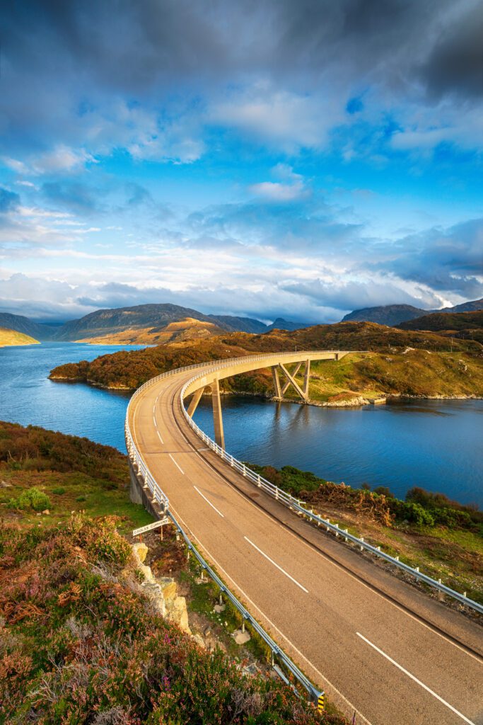 a road bridge over water with hills and mountains in the background